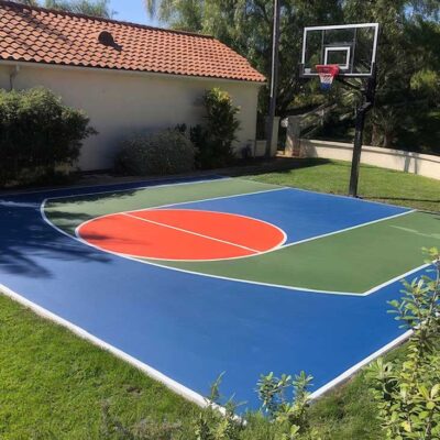 The Photo Shows A Gorgeous Blue, Green And Orange Basketball Half Court With White Striping In A Residential Backyard.