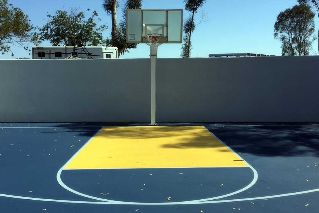 the photos shows a private residential basketball half court in blue and yellow colors with white striping.