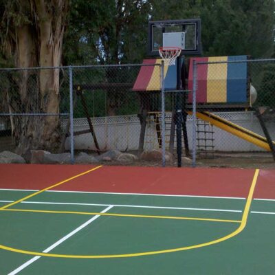 the photo shows yellow striping lines for a basketball court that was overlaid the end of a green tennis court, with white striping and red surround.