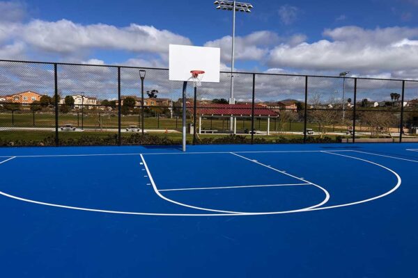 The Photo Shows The End Of A Full-sized Basketball Court In Bright Blue With White Striping.