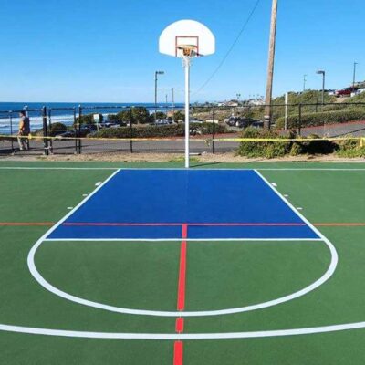 The Photo Shows The End Of A Multi-sport Full-size Basketball Court That Ferandell Tennis Courts Built For The Point Loma Nazarene University Using Green For The Court And Surround With White Lines, Plus Blue To Accent Specific Areas, And Overlaid Red Pickleball Lines.