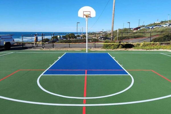 The Photo Shows The End Of A Multi-sport Full-size Basketball Court That Ferandell Tennis Courts Built For The Point Loma Nazarene University Using Green For The Court And Surround With White Lines, Plus Blue To Accent Specific Areas, And Overlaid Red Pickleball Lines.