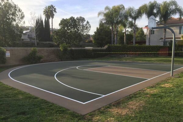 The Photo Shows A Basketball Half-court Designed In Forest Green And Beige With White Striping To Match The Beauty Of Its Surroundings.