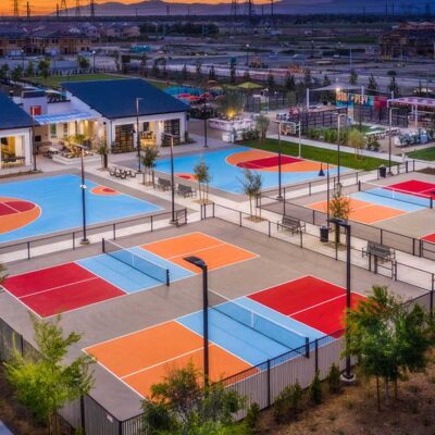 photo shows an aerial view of Canvas Park Community in Ontario California with four colorfully painted pickleball courts and two basketball courts using bright red, ice blue, and a fusion of yellow and orange, with white striping. Aerial photography provided by Frohlich Photography at CMFPhoto.com.