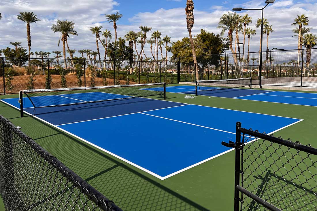 photo shows several light blue pickleball courts with darker blue kitchens and green surrounds at the desert horizon country club in indian wells.
