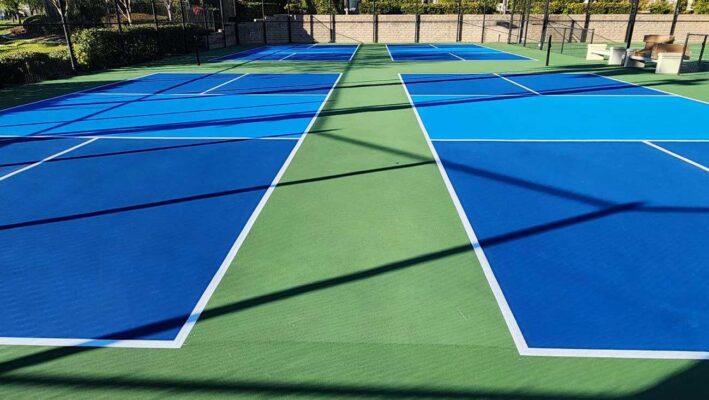 The Photo Shows Four Pickleball Courts Constructed By Ferandell Tennis Courts With Blue Courts, Light Blue Kitchens, White Striping, And Light Green Surrounds.