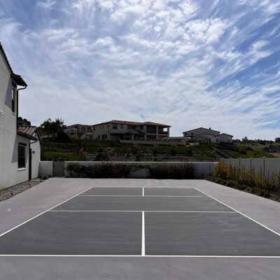 the photo shows a nice residence with a new pickleball court in gray with a dove gray surround built by ferandell tennis courts.
