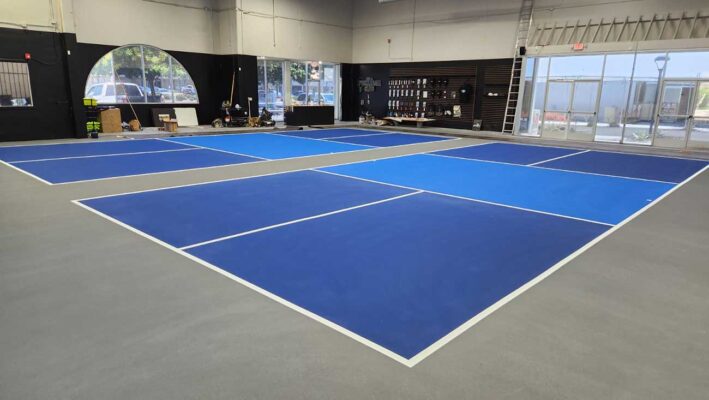 The Photo Shows Two Indoor Pickleball Courts Constructed By Ferandell Tennis Courts Using A Combination Of Blue And Light Blue For The Courts And Gray For The Surround.