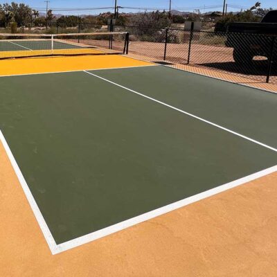 The Photo Shows A Residential Pickleball Court Painted In Forest Green With A Yellow Kitchen, White Striping And Sandstone Surround.