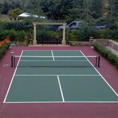 The photo shows a beautiful forest green pickleball court with a maroon surround built by Ferandell Tennis Courts