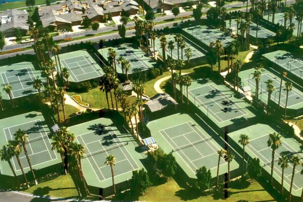 Photo Shows An Aerial View Of A Very Large Tennis Court Resort With Several Tennis Courts, Each Surrounded With Wind Screen Fencing.