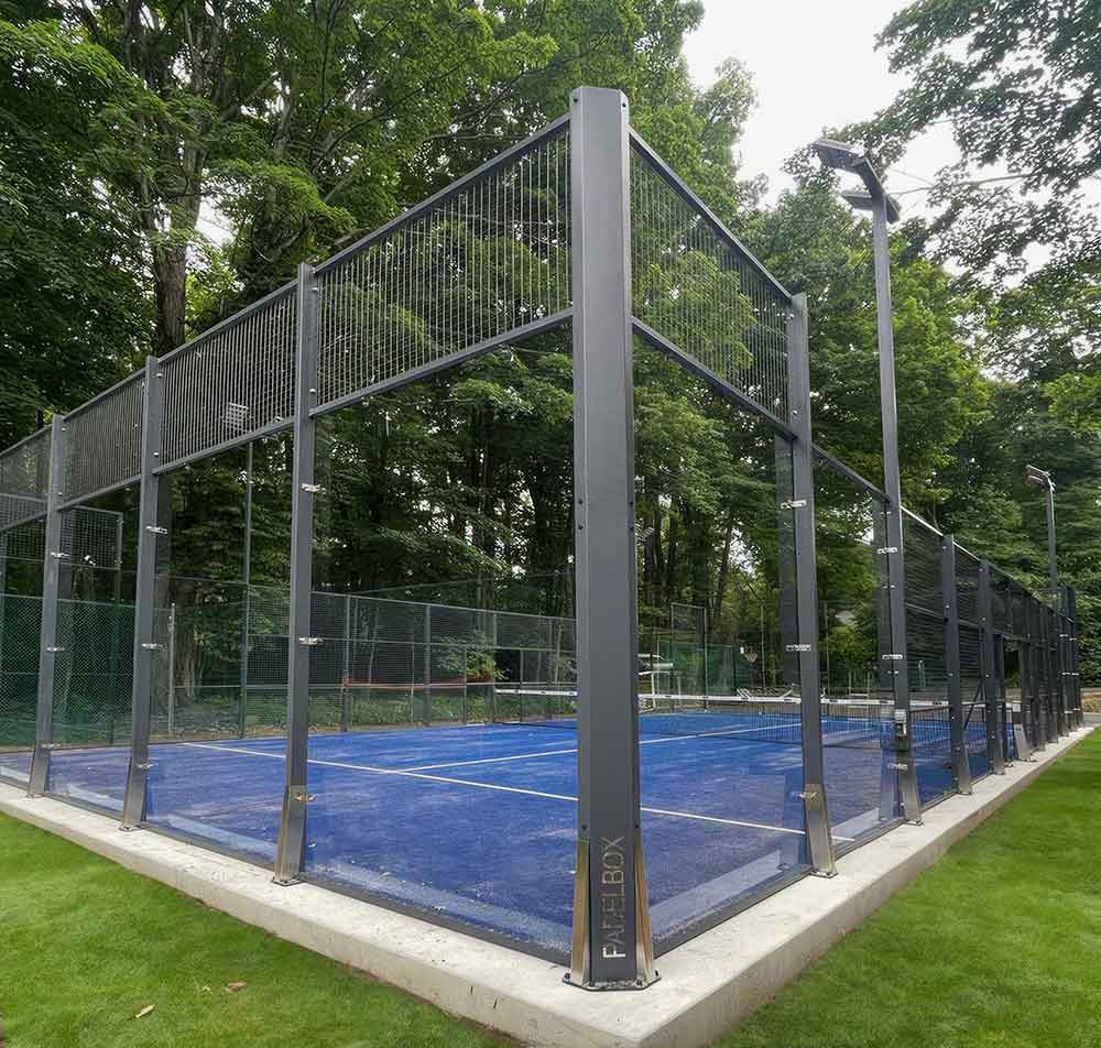 photo shows a padel court constructed with blue turf and black and glass enclosure.