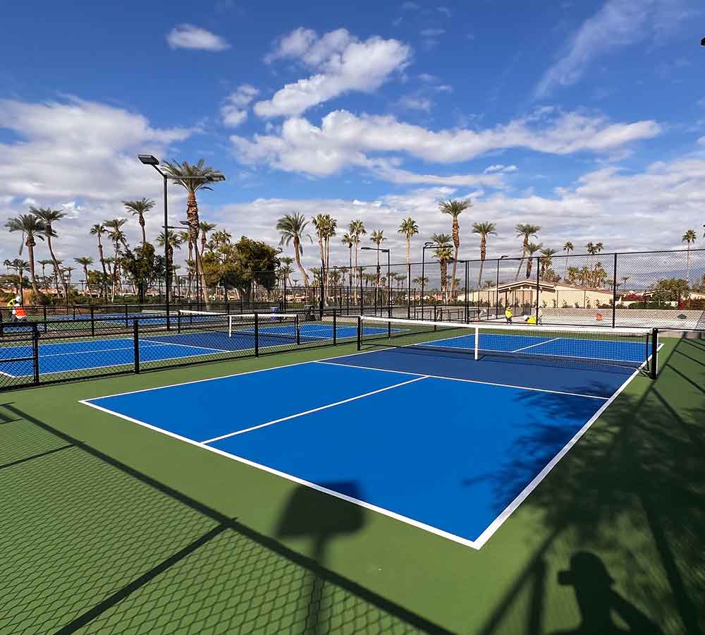 beautiful bright blue pickleball court with a green surround.